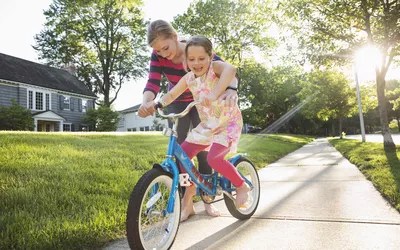 Babysitter teaching little girl how to ride a bike