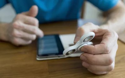 man holding fidget spinner while using smartphone